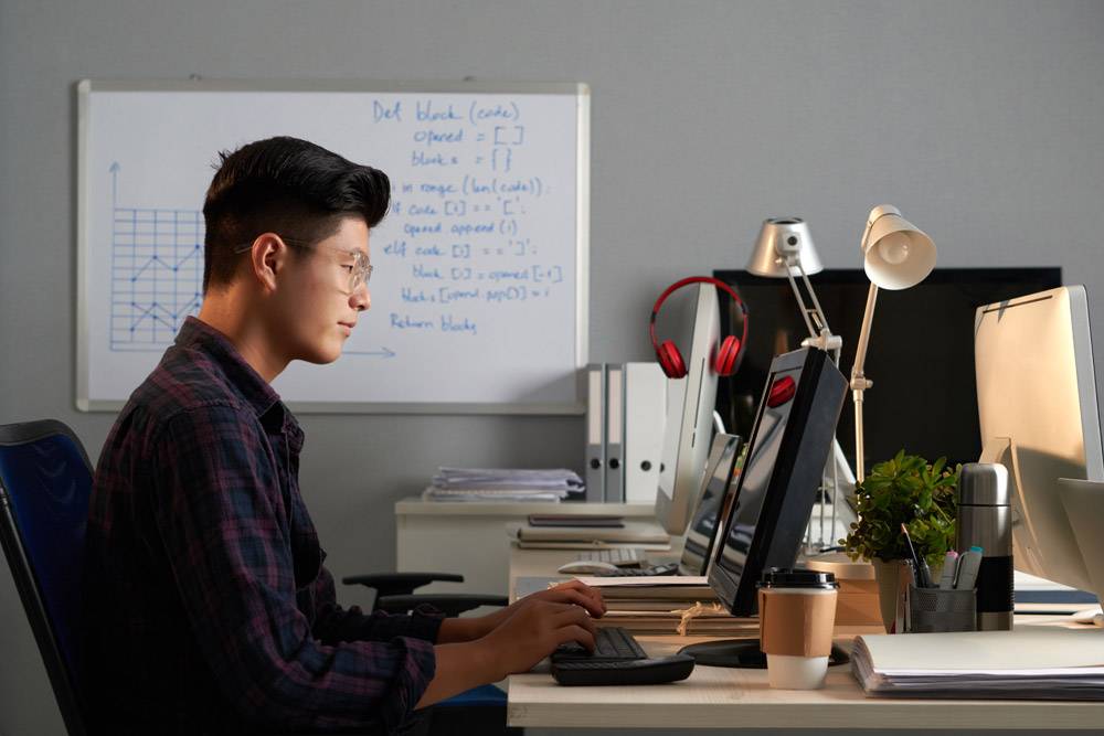 戴眼镜的年轻亚裔男子在办公室用电脑工作的_5576673