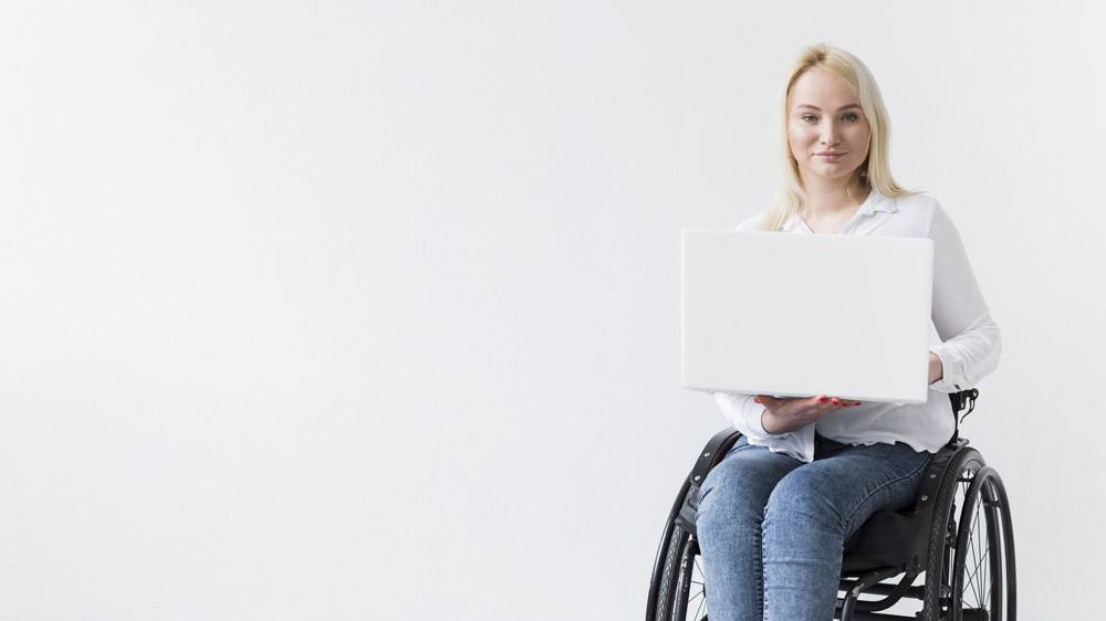坐在轮椅上的微笑女子在笔记本电脑上工作的_7772362