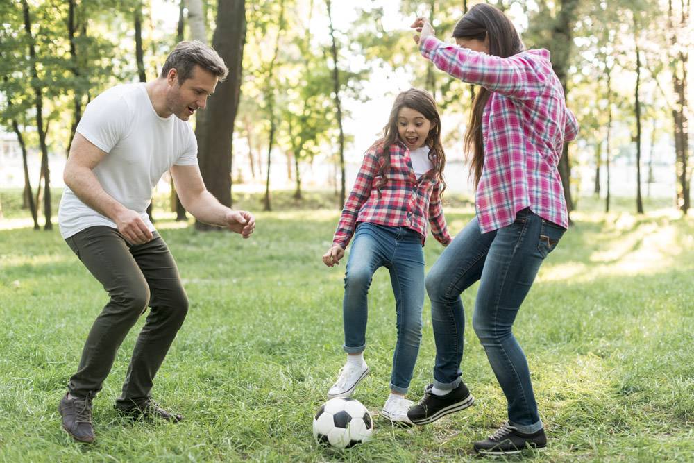 快乐的女孩和她的父母在公园的草地上踢足球_4958795