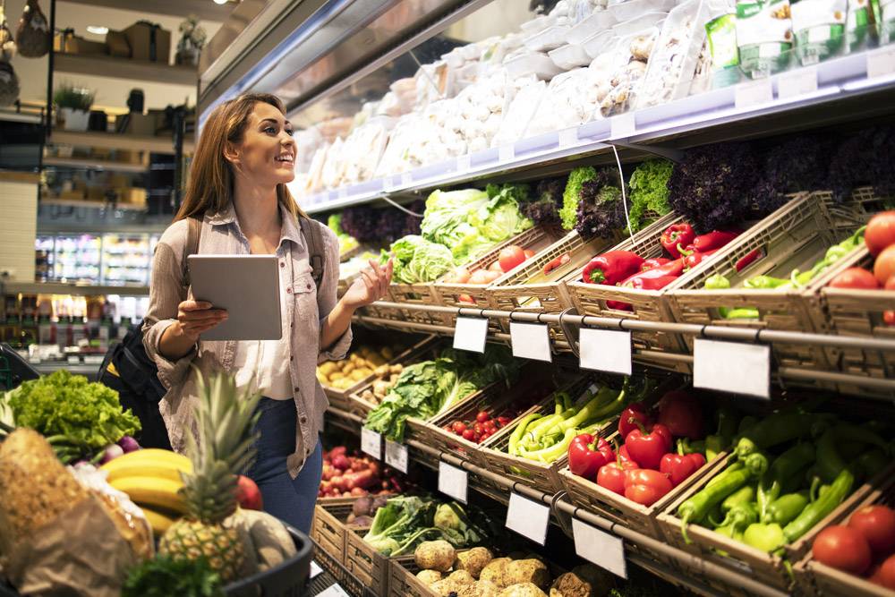 有片剂的妇女买健康食物在超级市场杂货店