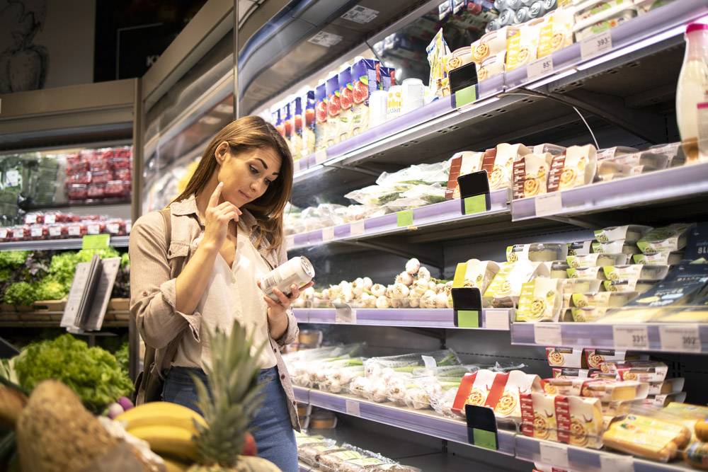 超级市场的妇女从架子从产品读取营养价值
